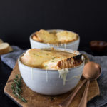 french onion soup with melted cheese on top in a gray bowl on a dark background