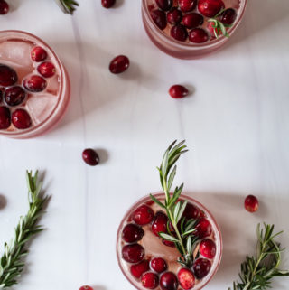 cranberry ginger gin fizz cocktails arranged on a white table topped with cranberries and fresh rosemary sprigs for garnish