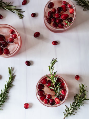 cranberry ginger gin fizz cocktails arranged on a white table topped with cranberries and fresh rosemary sprigs for garnish