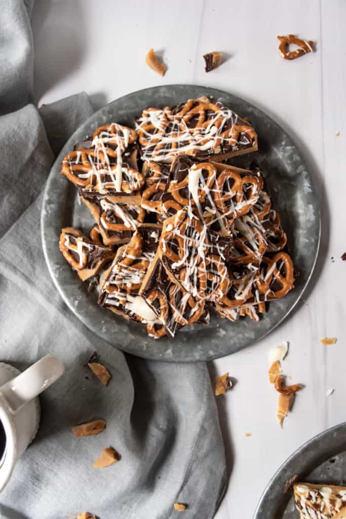two trays of butter toffee topped with chocolate, pretzels, and pecans