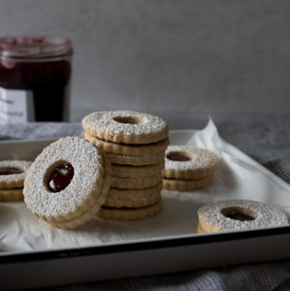 Stack of linzer cookies with raspberry jam in the center, dusted with confectioner's sugar