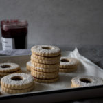stack of linzer cookies on a tray with jam and powdered sugar