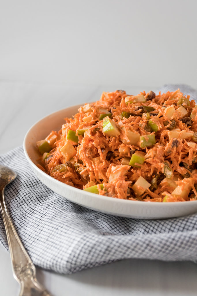 Vibrant carrot apple slaw served in a large white bowl.