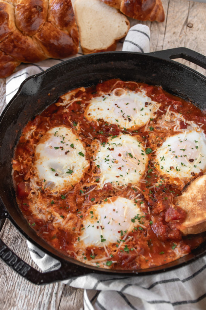 Eggs in Purgatory served in a a large cast iron skillet topped with basil and served with garlic toasts.