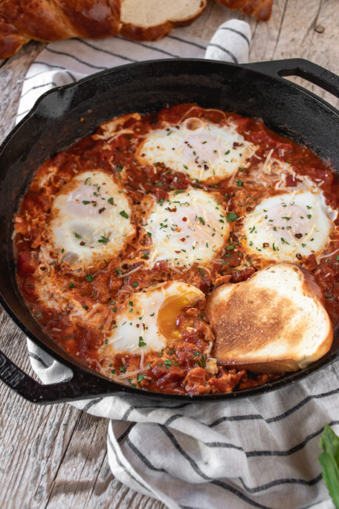Eggs in Purgatory served in a a large cast iron skillet topped with basil and served with garlic toasts.