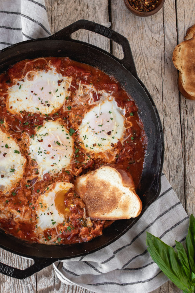 Eggs in Purgatory served in a a large cast iron skillet topped with basil and served with garlic toasts. Runny yolks to sop up with the toast.