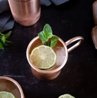 ginger gin mule cocktail served in frosty copper mug topped with lime wedge and sprigs of mint