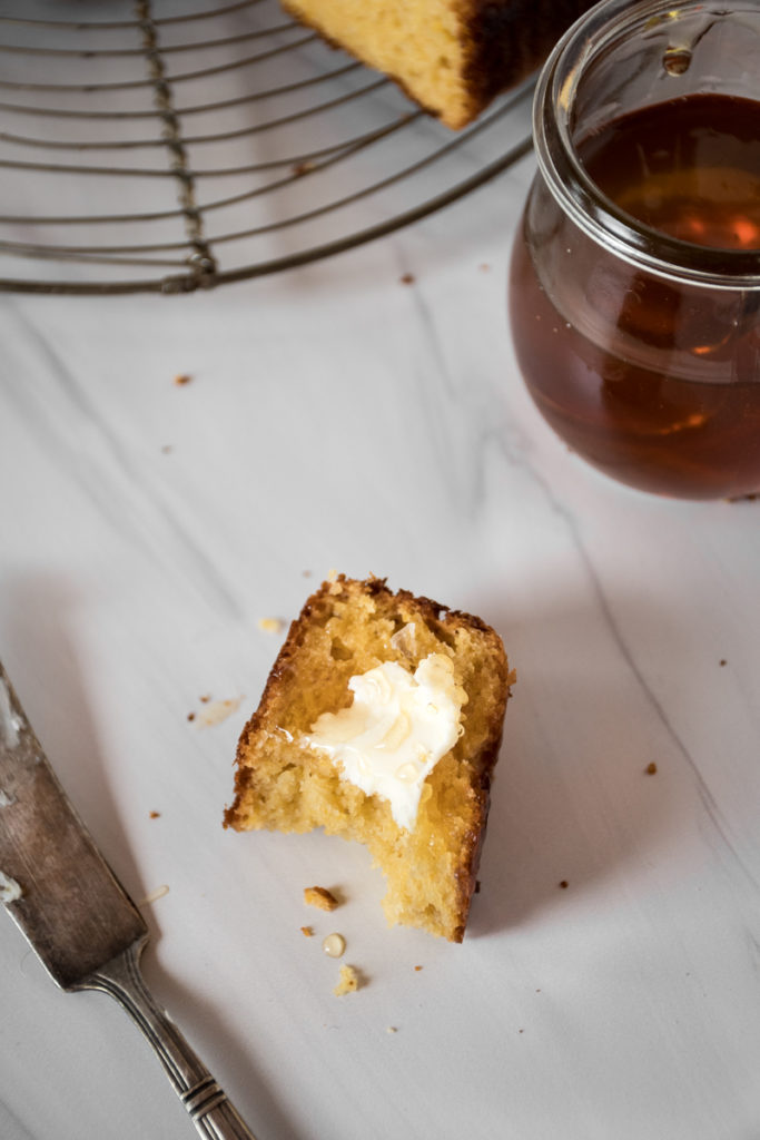 Slice of sweet cornbread with butter and honey, bite taken out, crumbs 