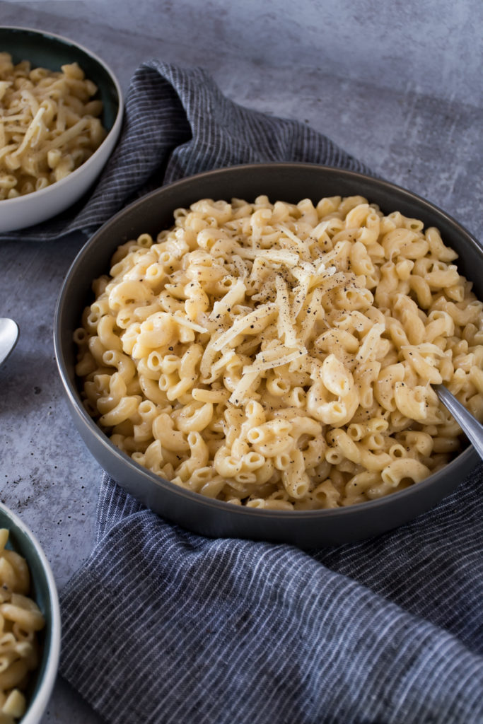 Creamy three cheese macaroni made in an instant pot served in a large gray bowl topped with grated white cheddar cheese