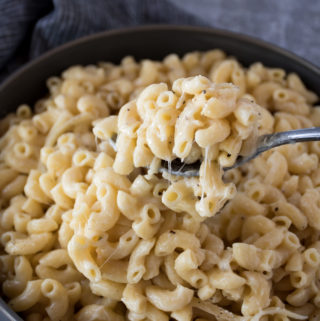 Creamy three cheese macaroni made in an instant pot served in a large gray bowl topped with grated white cheddar cheese