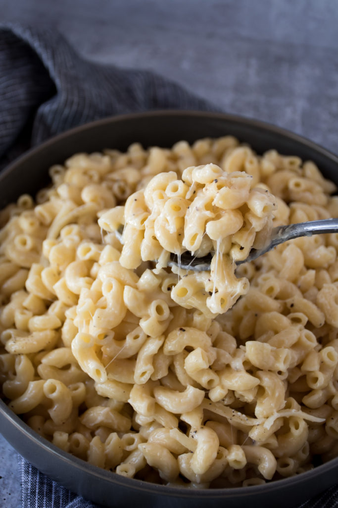 Creamy three cheese macaroni made in an instant pot served in a large gray bowl topped with grated white cheddar cheese