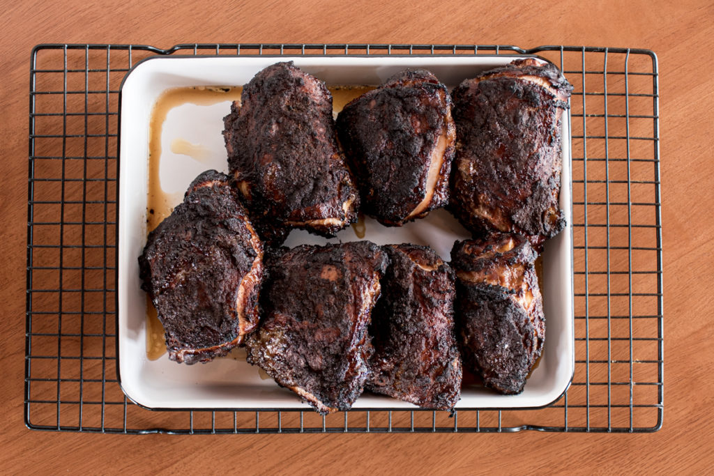 blackened jamaican jerk chicken thighs arranged on a white tray prior to serving, just removed from charcoal grill