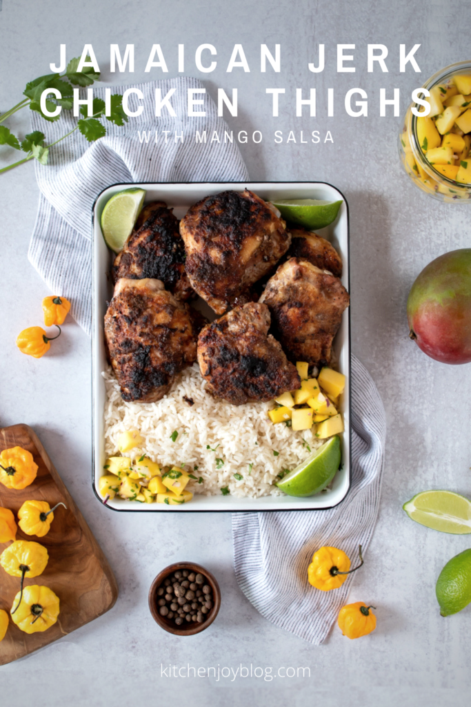 Jamaican Jerk Chicken Thighs with Mango salsa, image shows how the final product should look with crispy skin, served with rice and mango salsa, also scotch bonnet peppers, limes, and mangoes in the scene