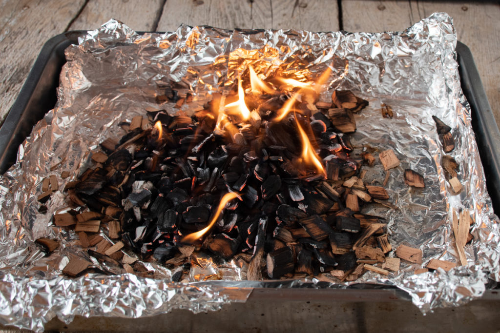 roasting pan lined with foil, filled with flaming pimento wood chips for smoking jerk chicken in the oven