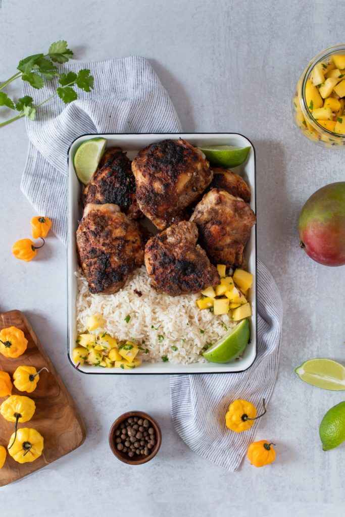 jamaican jerk chicken thighs with blackened crispy skin, smoked on a charcoal grill or in the oven, served on a platter with rice and mango salsa
