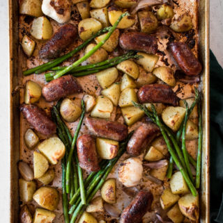 Large tray of crispy, golden sheet pan sausages and potatoes with garlic and asparagus