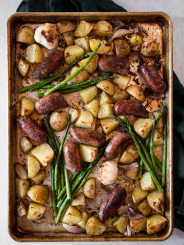 Large tray of crispy, golden sheet pan sausages and potatoes with garlic and asparagus