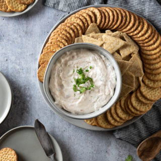 Creamy smoked salmon dip sprinkled with dill and green onions served with a platter of crackers on a gray tray.