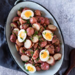 warm potato salad made from red potaotes, bacon, shallots, dijon, and green onions, topped with soft boiled eggs