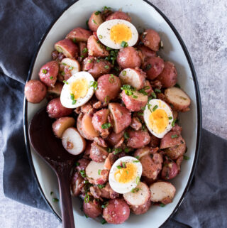 warm potato salad made from red potatoes, served on a blue platter and topped with soft boiled eggs and green onions.