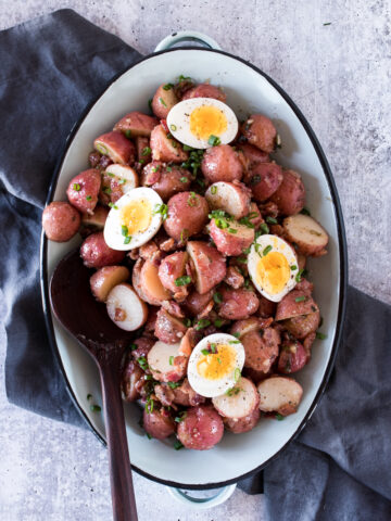 warm potato salad made from red potatoes, served on a blue platter and topped with soft boiled eggs and green onions.