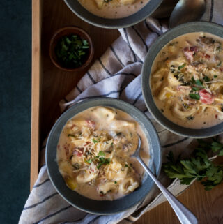 3 bowls of creamy tortellini and sausage soup on a wooden tray