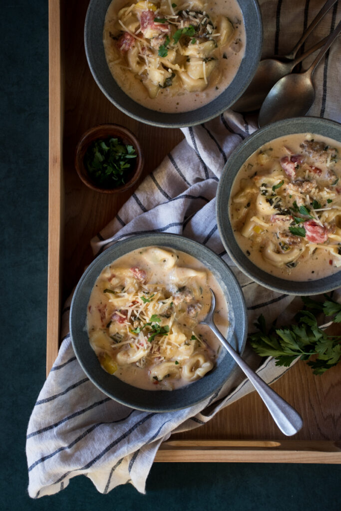 3 bowls of creamy tortellini and sausage soup on a wooden tray
