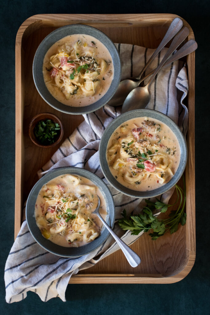 three bowls of creamy sausage and tortellini soup on a wooden tray