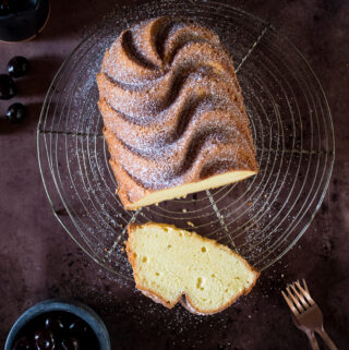 Golden pound cake dusted with powdered sugar cooling on a rack. A slice is cut out to reveal the light textured, buttery interior.
