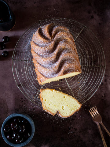 Golden pound cake dusted with powdered sugar cooling on a rack. A slice is cut out to reveal the light textured, buttery interior.