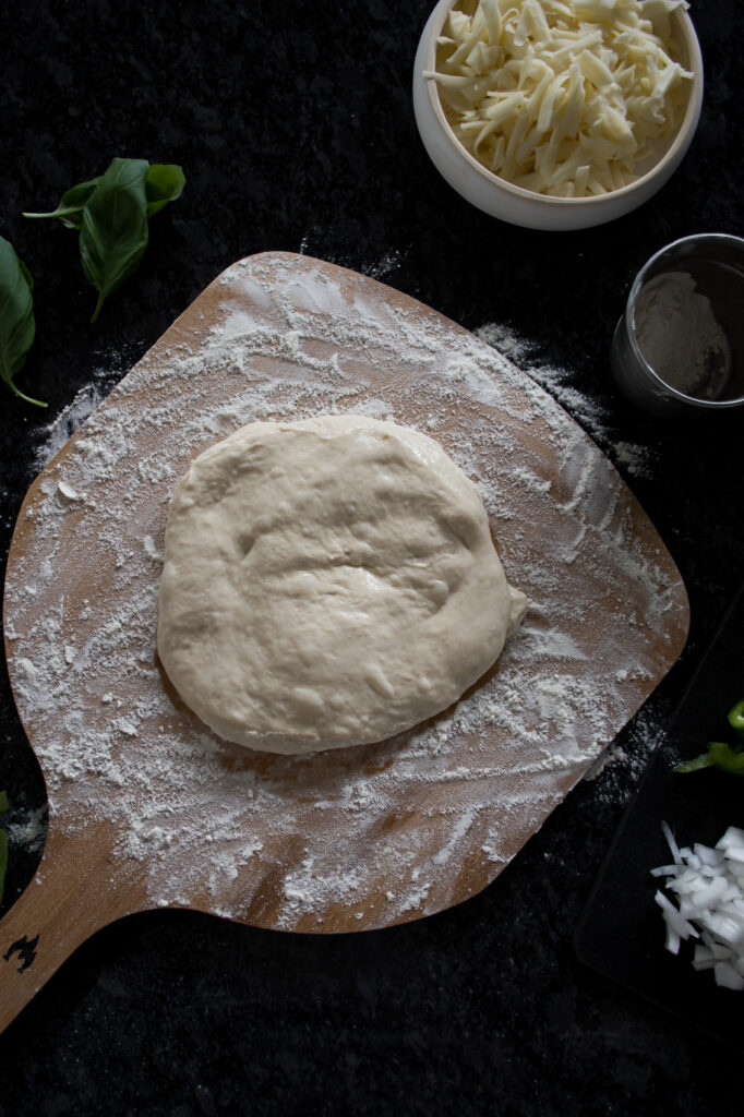sourdough pizza dough resting on a floured pizza peel ready to shape into pizza