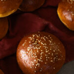close up view of sweet potato sourdough buns to show golden, shiny crust dotted with sesame seeds