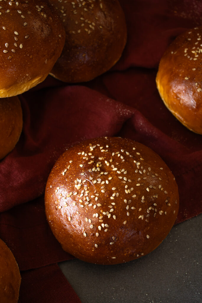 close up view of sweet potato sourdough buns to show golden, shiny crust dotted with sesame seeds
