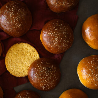 homemade sweet potato sourdough buns topped with sesame seeds, one is sliced to reveal the golden, soft interior