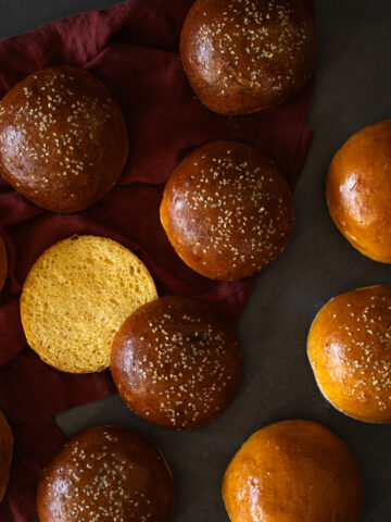homemade sweet potato sourdough buns topped with sesame seeds, one is sliced to reveal the golden, soft interior