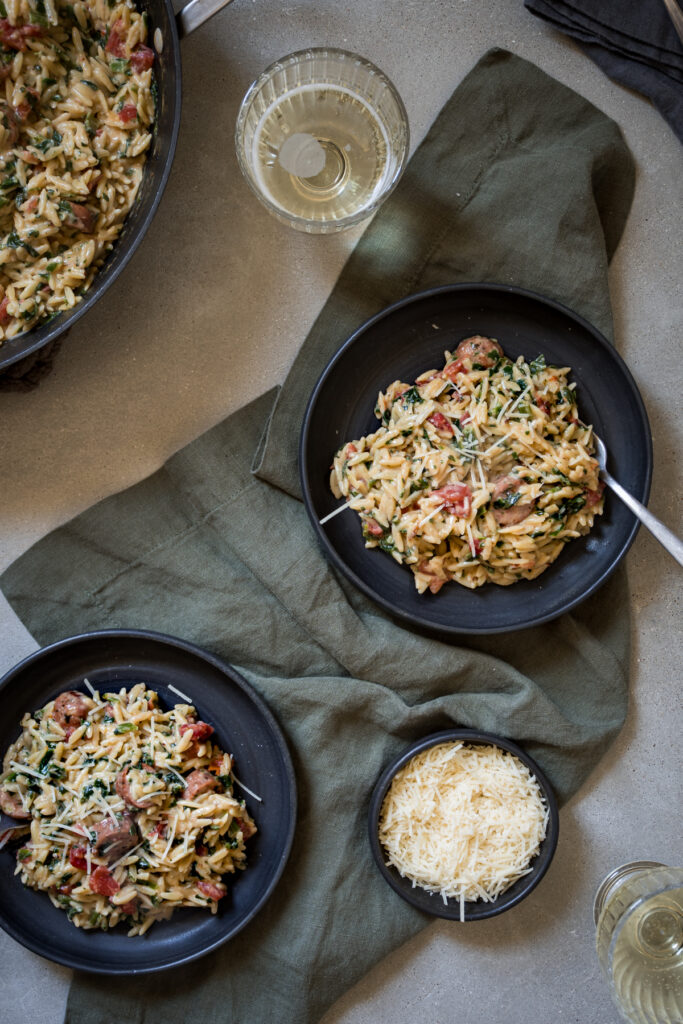 two black bowls filled with creamy one-pot orzo with spinach and tomatoes and Italian sausage